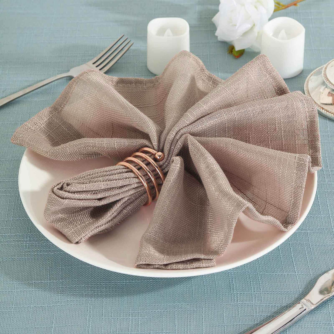 Elegant taupe napkin with copper ring elegantly arranged on a plate.