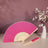 Pink folding fan with cream accents next to a vase of white flowers.