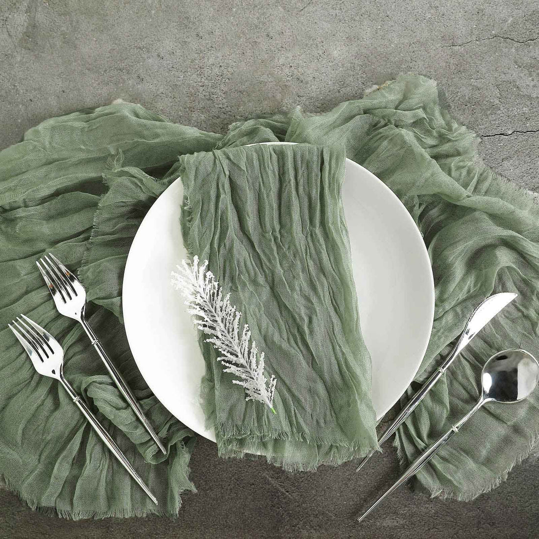 Elegant green linen napkin on a white plate with silver cutlery on textured surface.