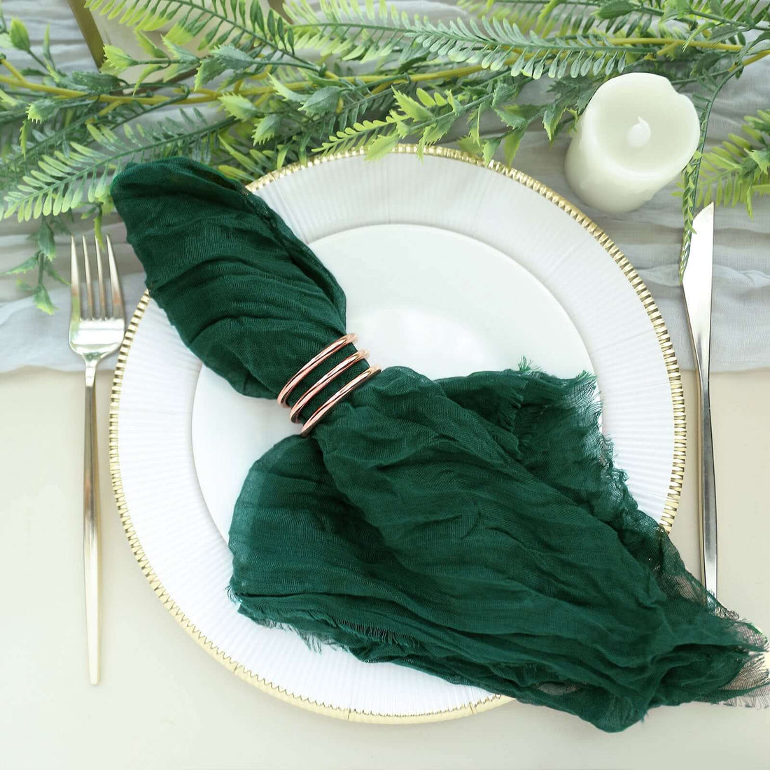 Elegant green napkin with gold rings on a plate, styled with greenery and candle.