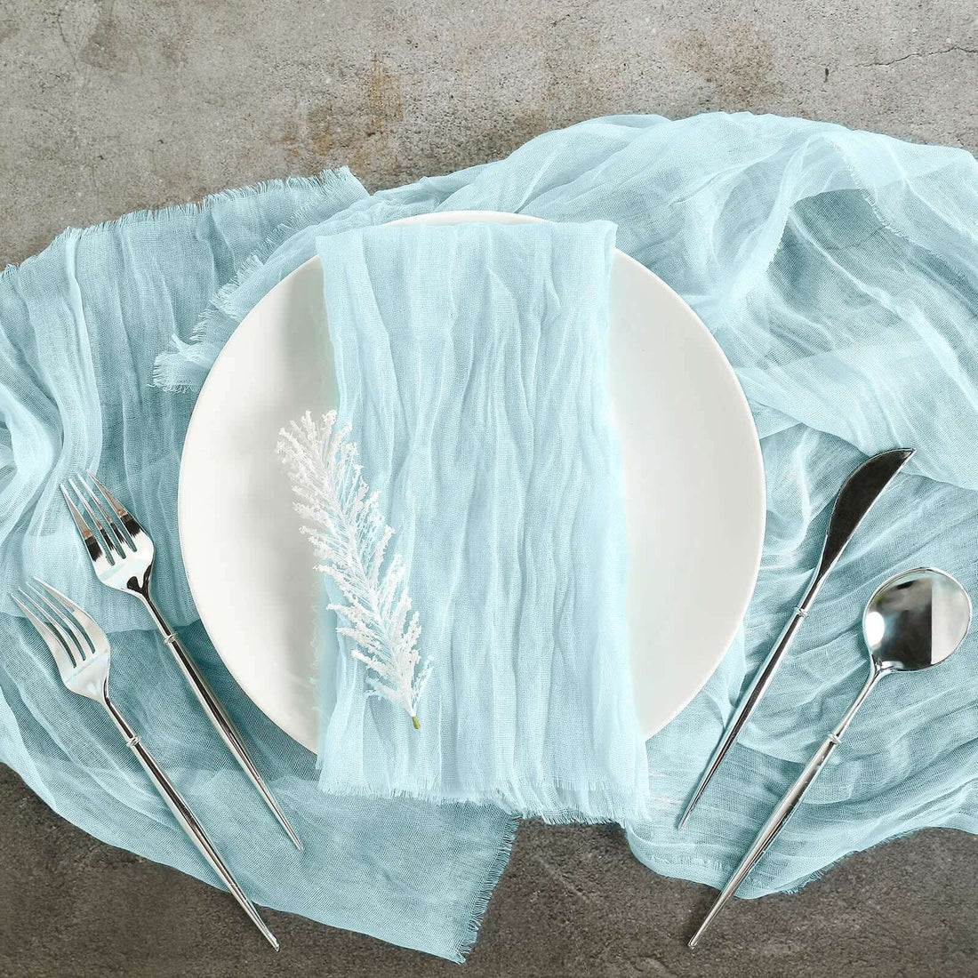 Light blue table runner with white plate and silver cutlery on a textured surface.
