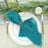Teal napkin with gold rings on a white plate, surrounded by greenery and candles.