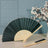 Elegant green folding fan with wooden handle and matching comb on a table.