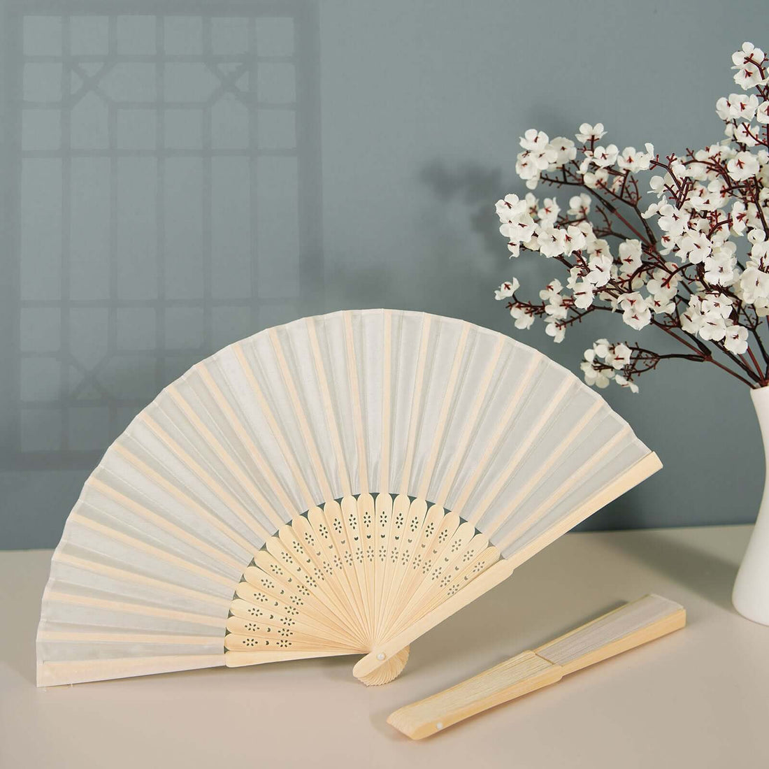 Decorative folding fan with intricate design and wooden handle, styled with flowers.
