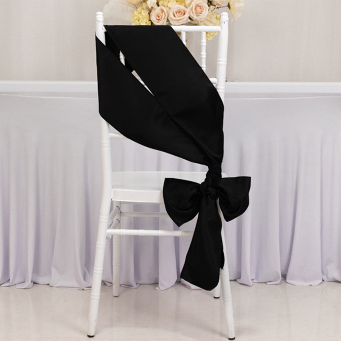 Black satin chair sash tied in a bow on a white chair.