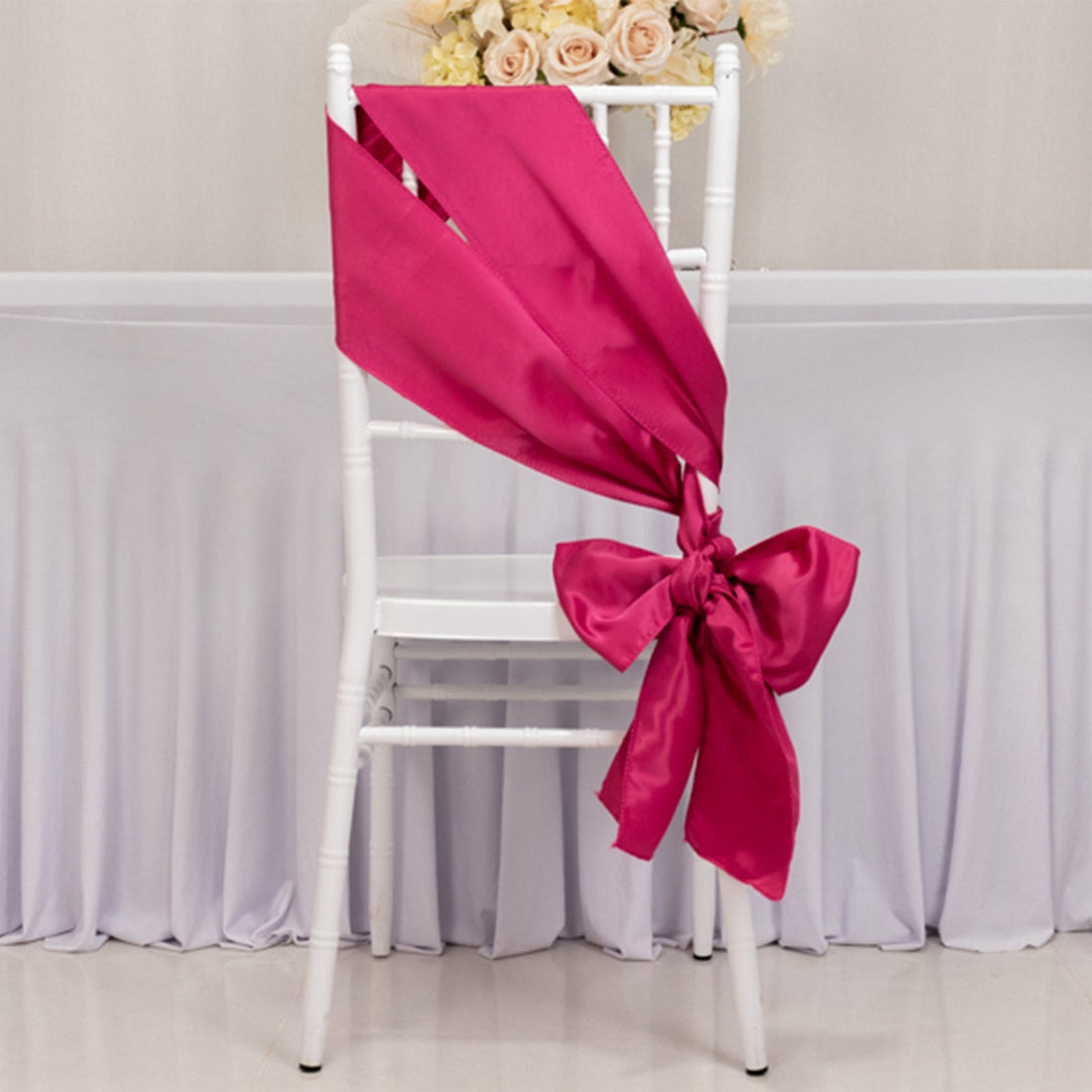 Hot pink satin chair sash tied in a bow on a white chair.