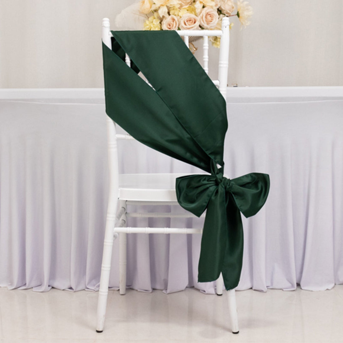 Dark green satin chair sash elegantly tied in a bow on a white chair.