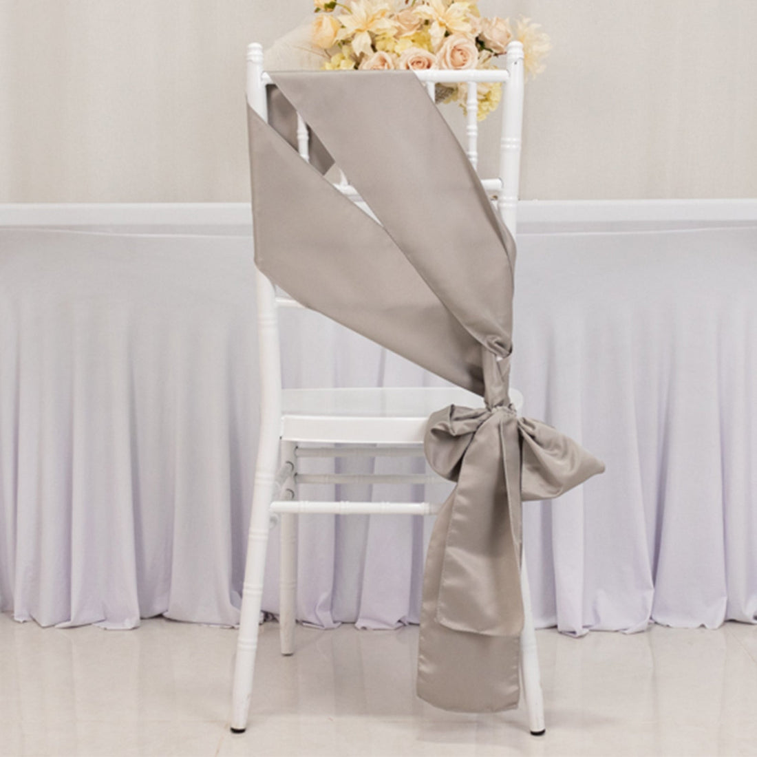 Elegant beige satin chair sash tied in a bow on a white chair.