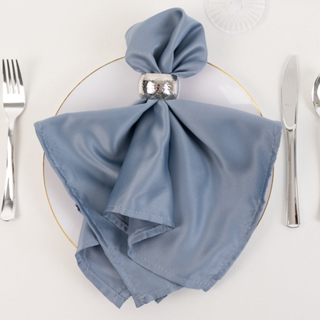 Blue satin napkin elegantly styled on a plate with a silver napkin ring.