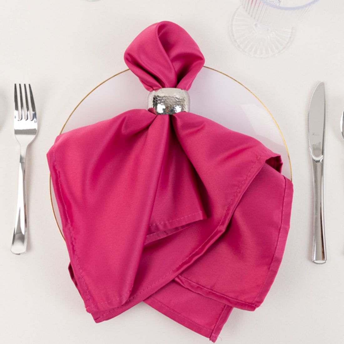 Pink napkin elegantly folded on a plate with silver napkin ring.