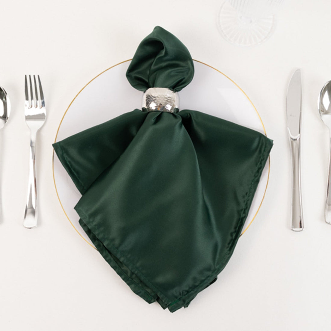 Green satin napkin elegantly styled on a plate with silver napkin ring.