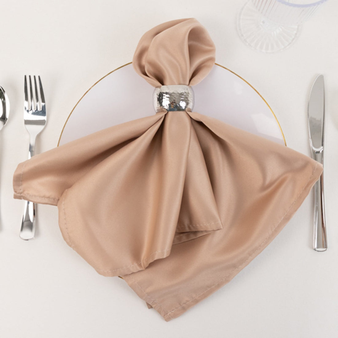 Elegant beige satin napkin with silver ring on a white plate.