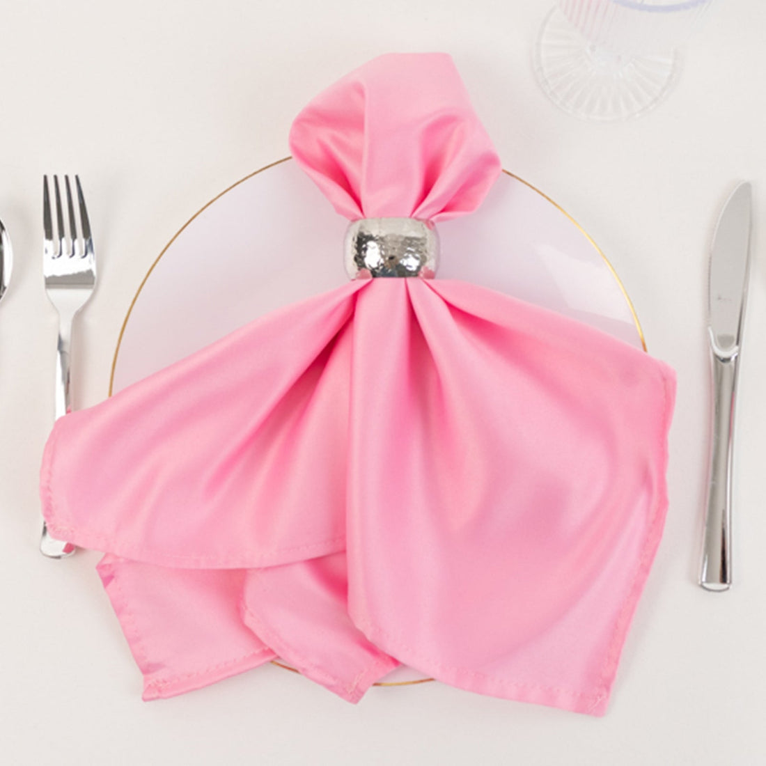 Pink satin napkin tied elegantly with a silver napkin ring on a white plate.