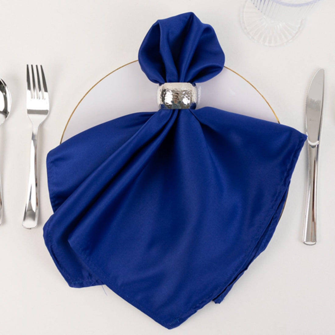 Elegant blue napkin elegantly arranged on a plate with a silver napkin ring.