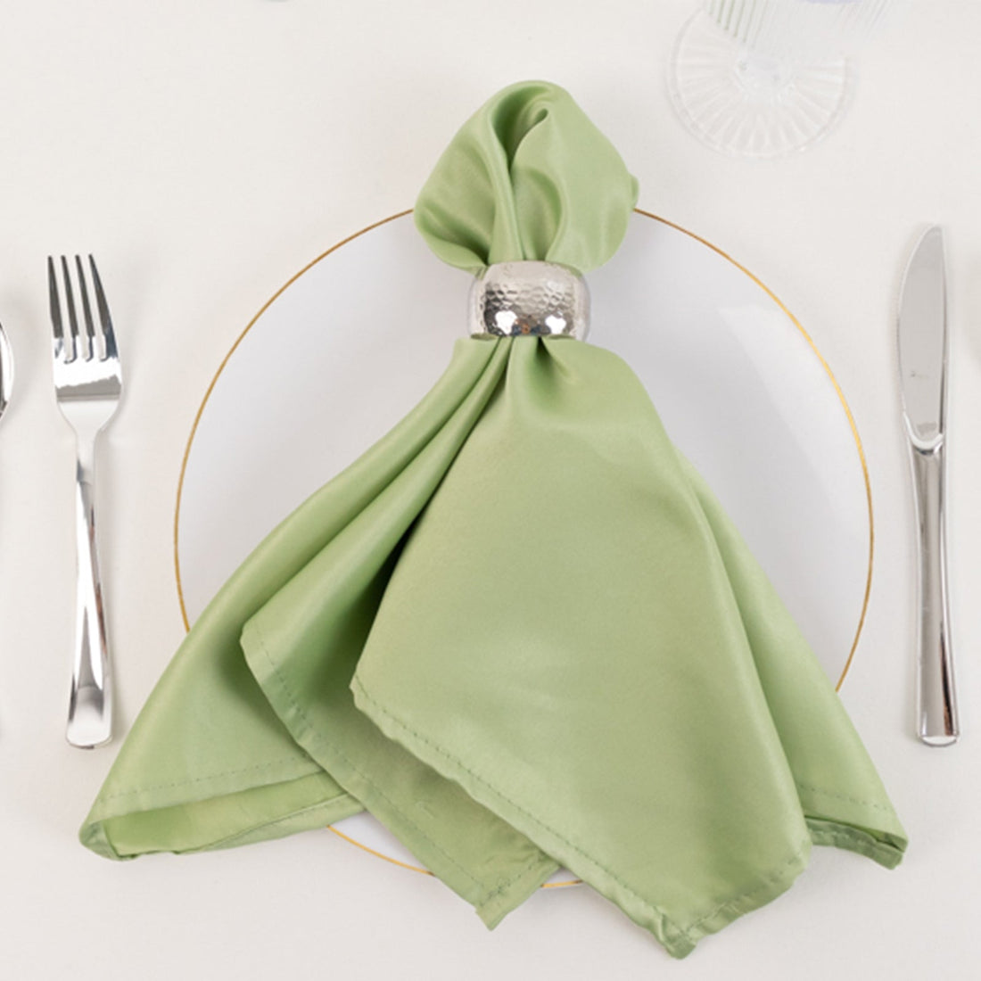 Green napkin elegantly tied with a silver ring on a white plate with cutlery.