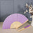 Purple folding fan displayed with a vase and flowers in a stylish setting.