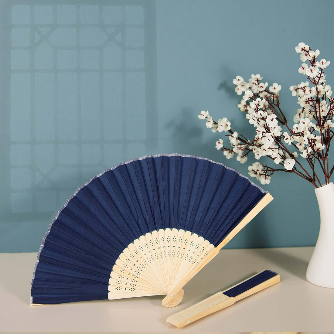 Navy blue folding fan with wooden handle and decorative pattern against a soft background.