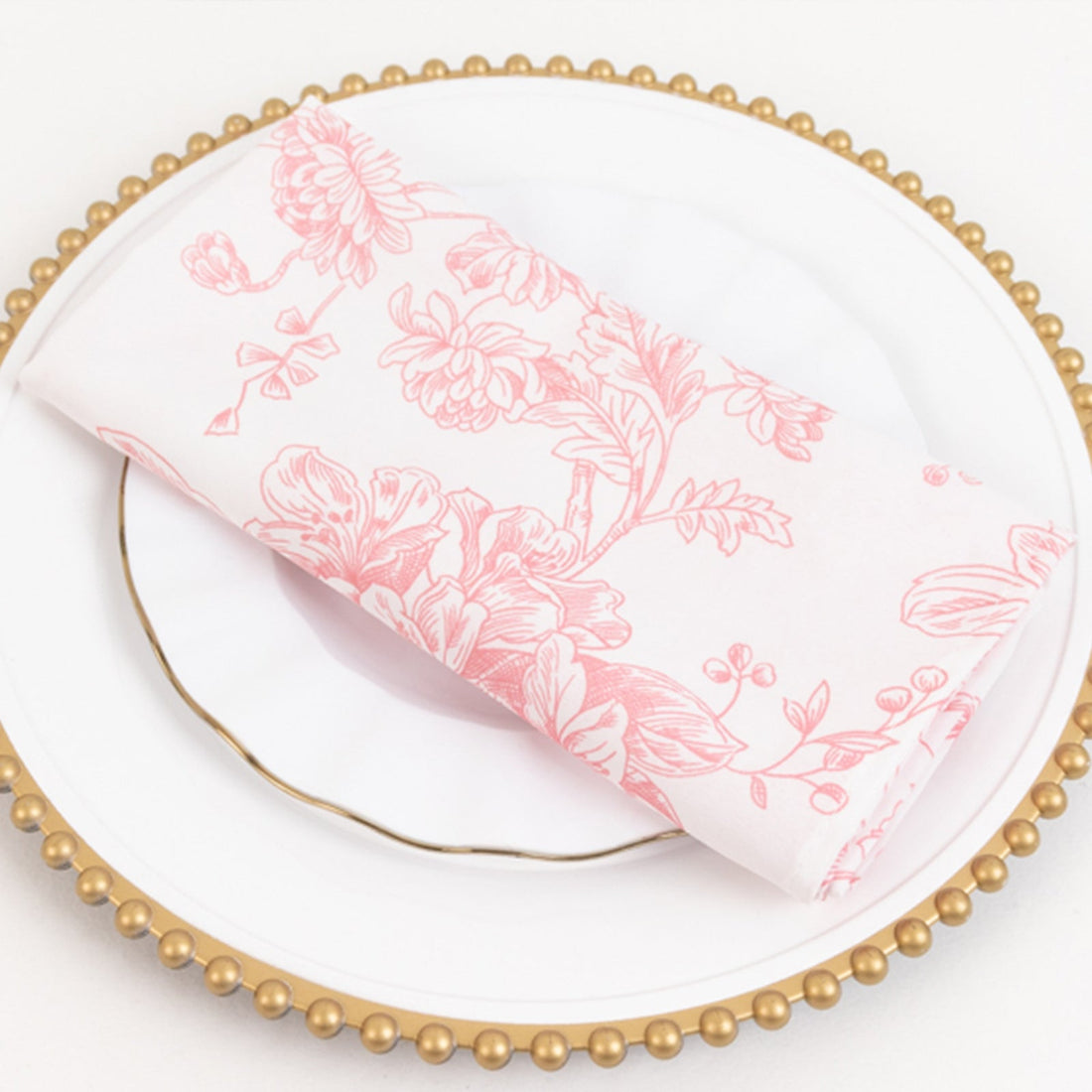 Pink floral napkin on a decorative gold-rimmed plate.