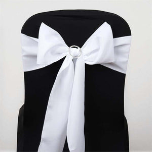 White satin chair sash with bow and rhinestone detail on black chair.