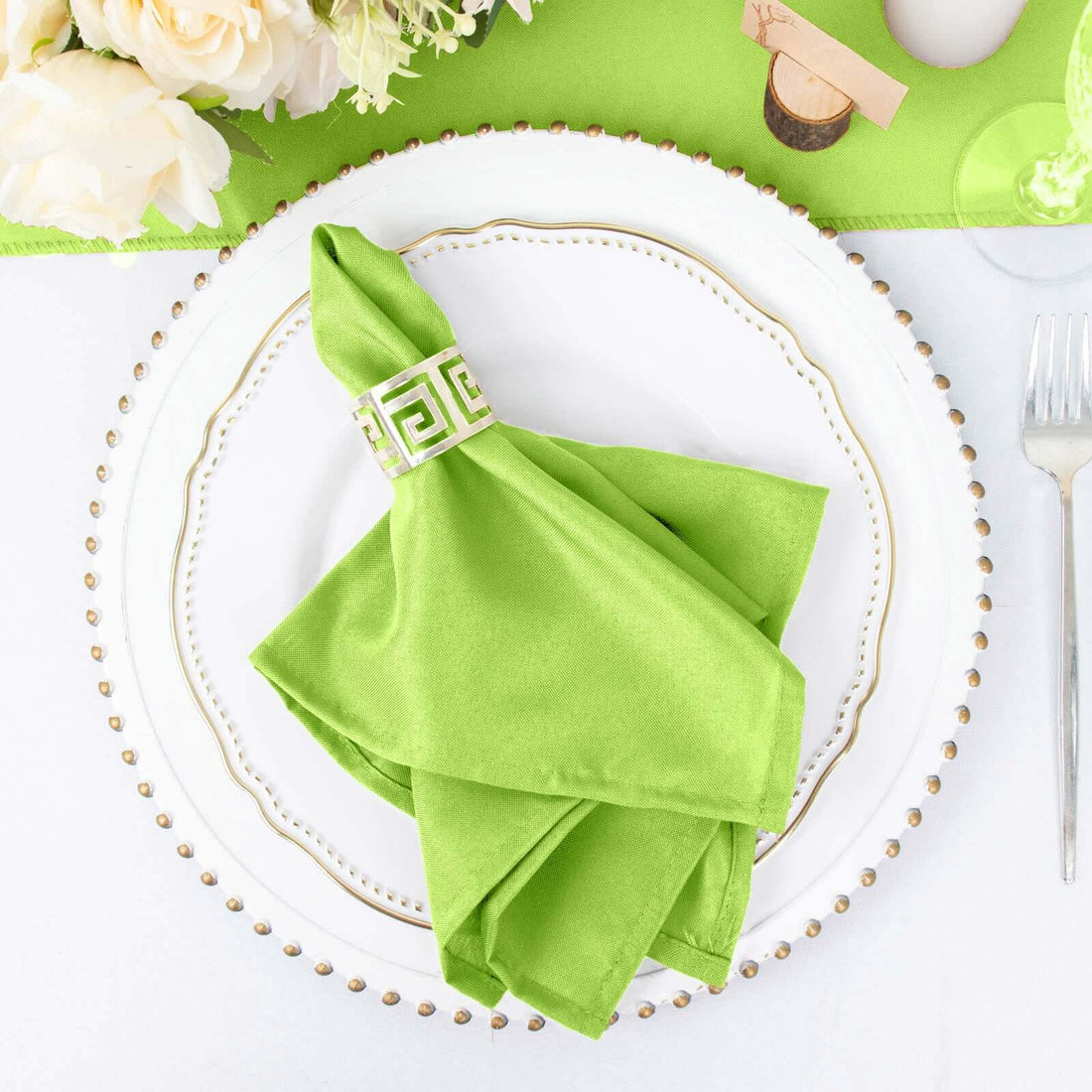 Green napkin with decorative ring on a white plate, styled for an elegant table setting.