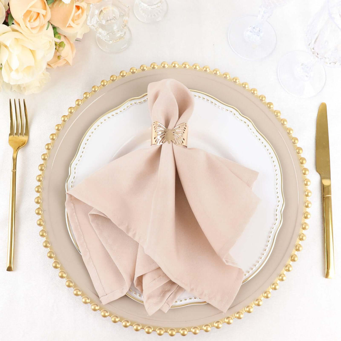 Elegant beige napkin with gold holder on a decorative plate, set for a formal dining experience.