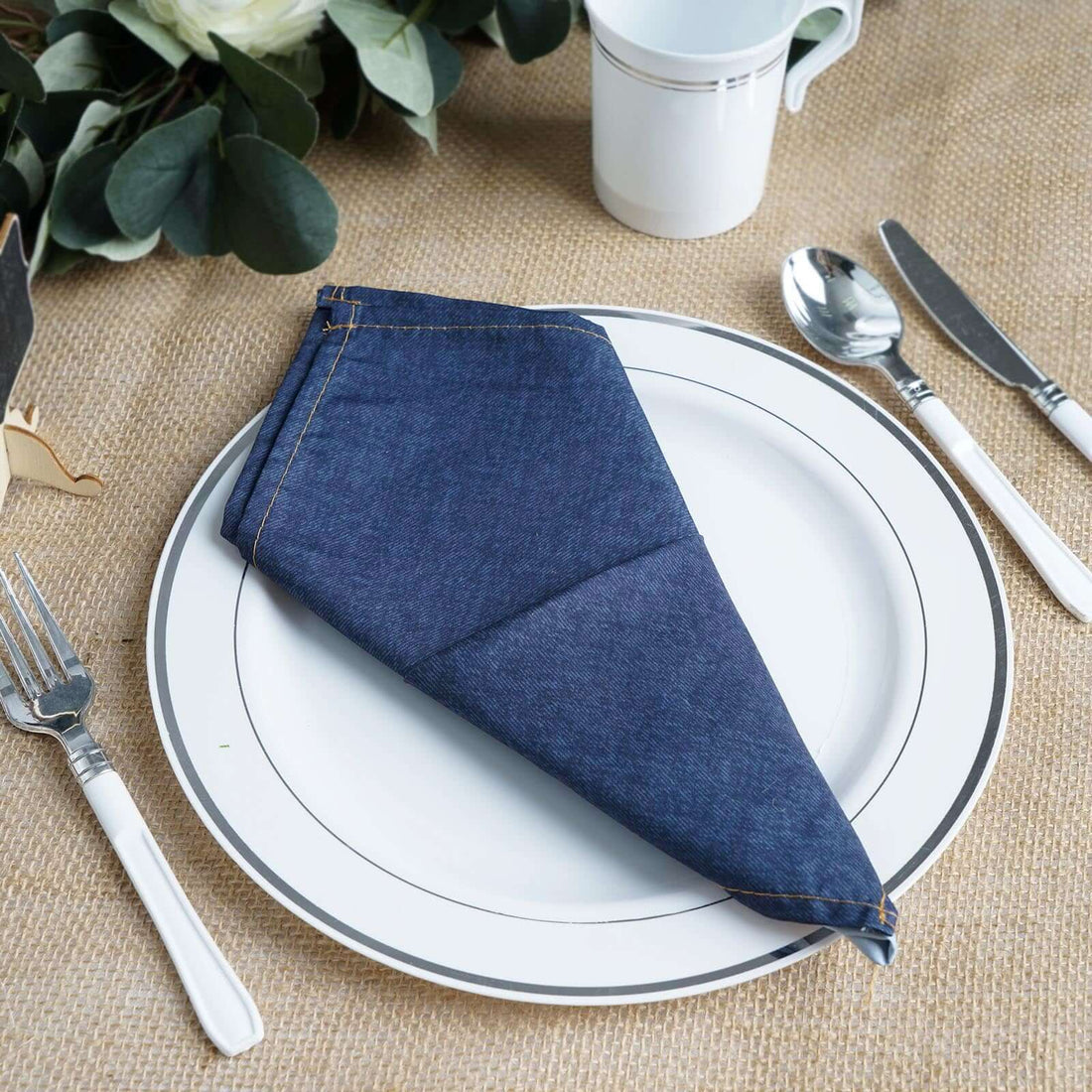 Denim napkin elegantly folded on a white plate with cutlery.