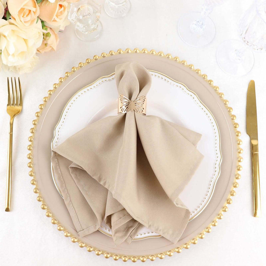 Elegant beige napkin with decorative ring on a stylish dinner plate setting.
