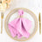 Pink napkin with gold holder on a decorative plate, elegantly set for dining.