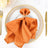 Elegant orange napkin with butterfly ring on a decorative plate.