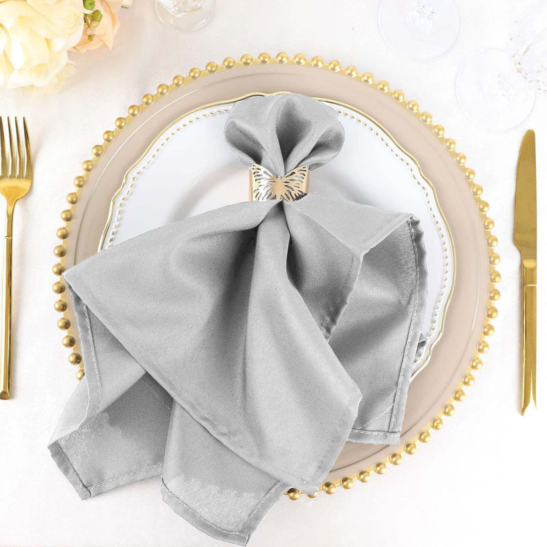 Elegant silver napkin folded on a decorative plate with gold beaded rim.