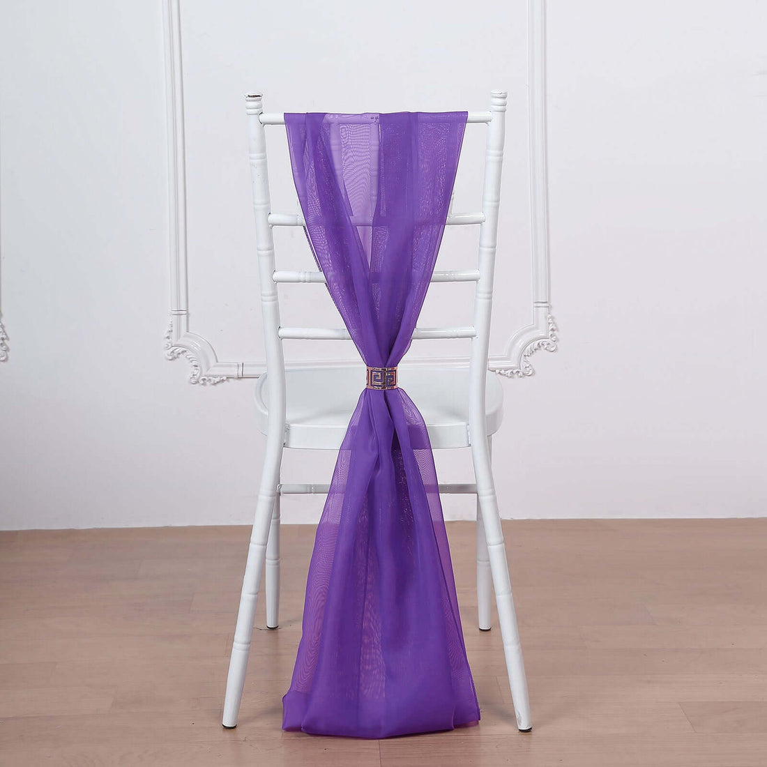 Purple chair sash tied on a white chair against a plain backdrop.