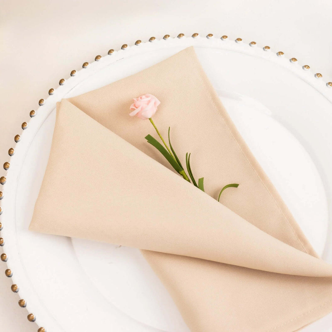 Elegant beige napkin folded with a pink flower on a decorative plate.