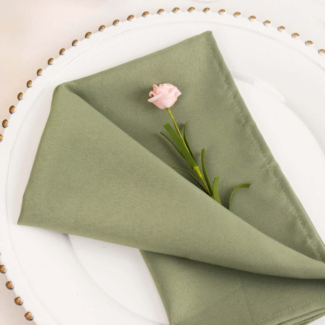Green napkin with a pink rose on a decorative plate.
