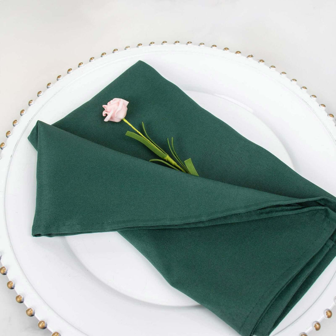 Green napkin elegantly folded on a decorative plate with a pink flower accent.