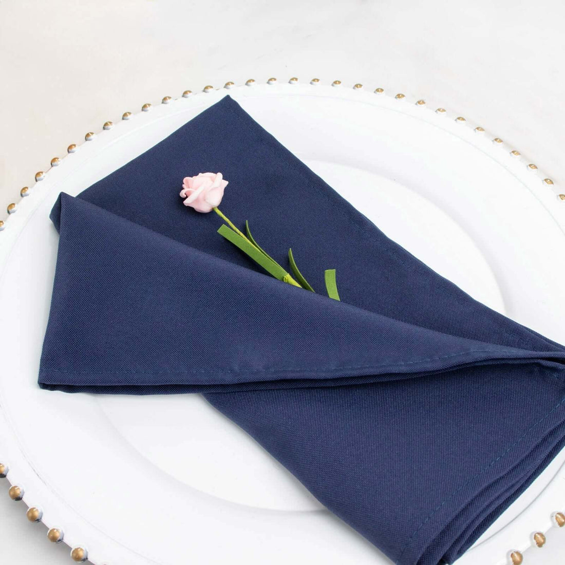 Navy blue napkin elegantly folded with a pink flower on a white plate.