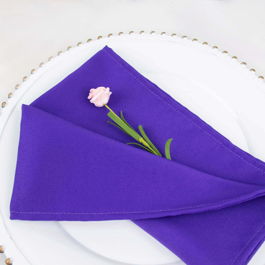 Purple napkin elegantly folded on a white plate with a pink flower accent.