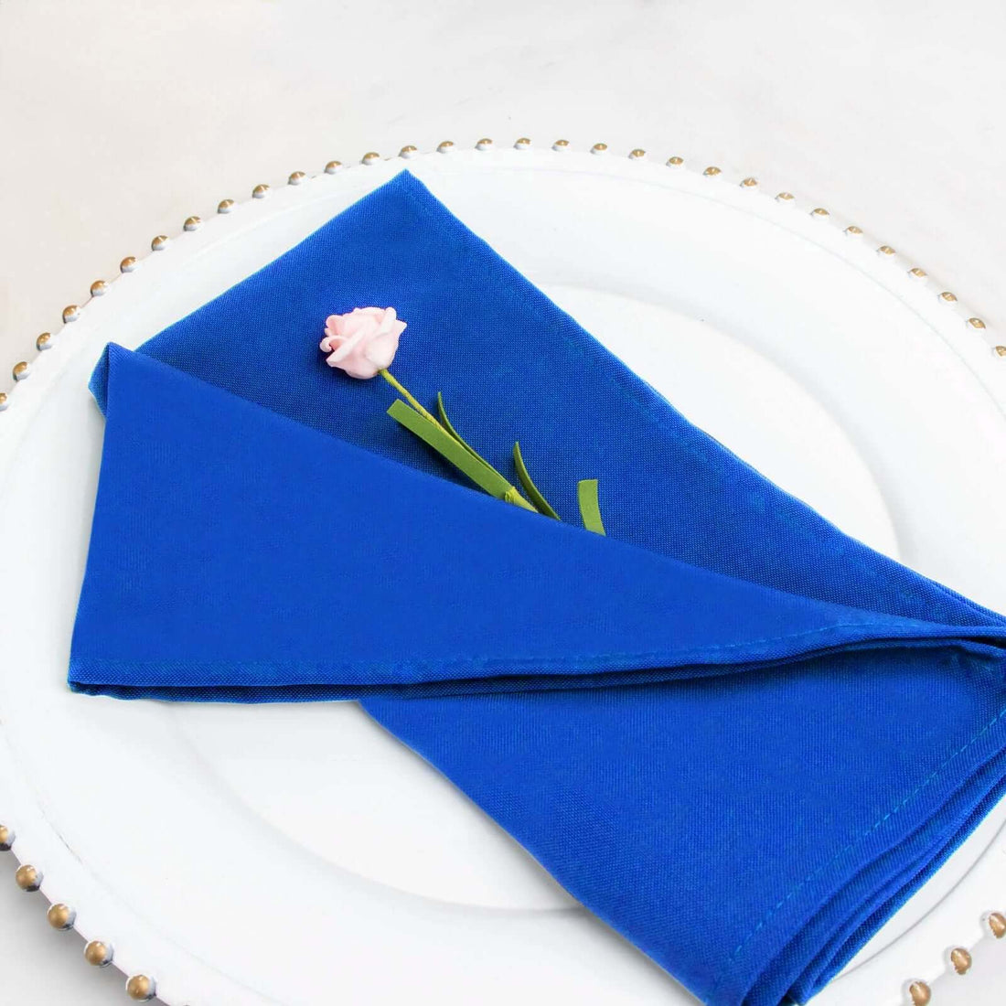 Blue cloth napkin elegantly folded with a pink flower on a white plate.