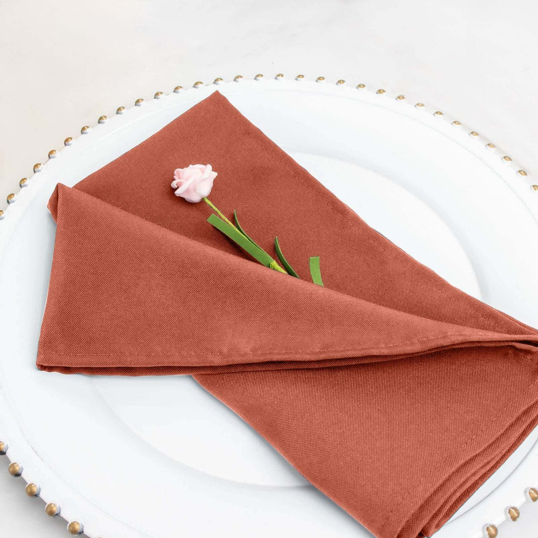 Rust-colored napkin elegantly folded with a pink flower accent