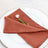 Rust-colored napkin elegantly folded with a pink flower accent
