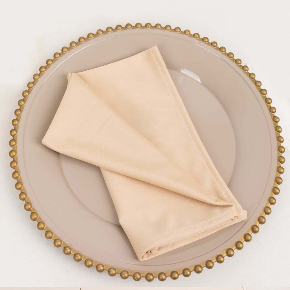 Beige cloth napkin folded on an elegant plate with a gold beaded rim.