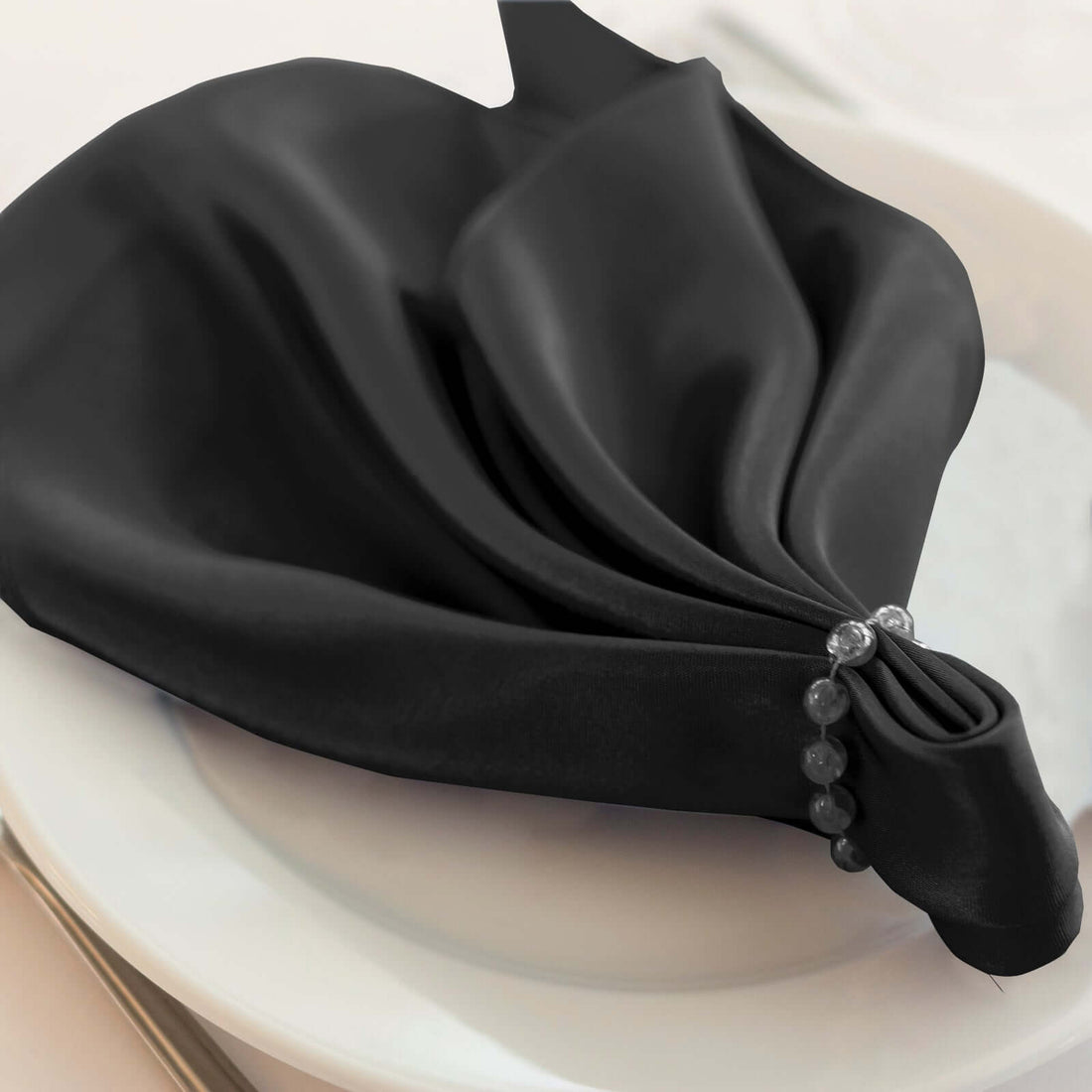 Elegant black napkin styled with beads on a white plate.