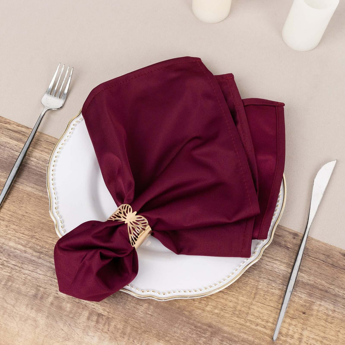 Burgundy fabric napkin elegantly styled on a white plate with cutlery.