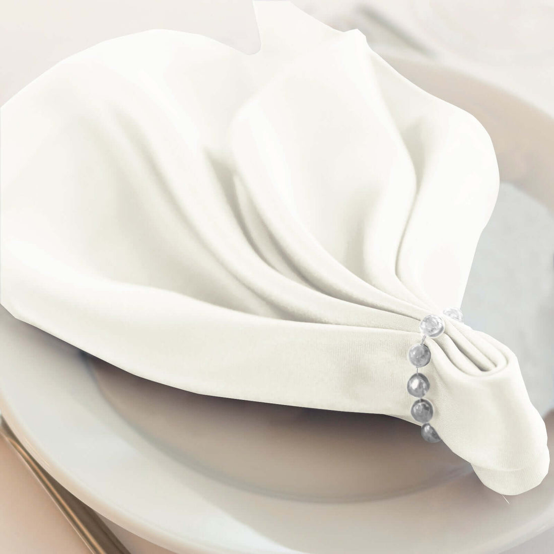 Elegant white napkin elegantly folded on a plate with decorative beads.
