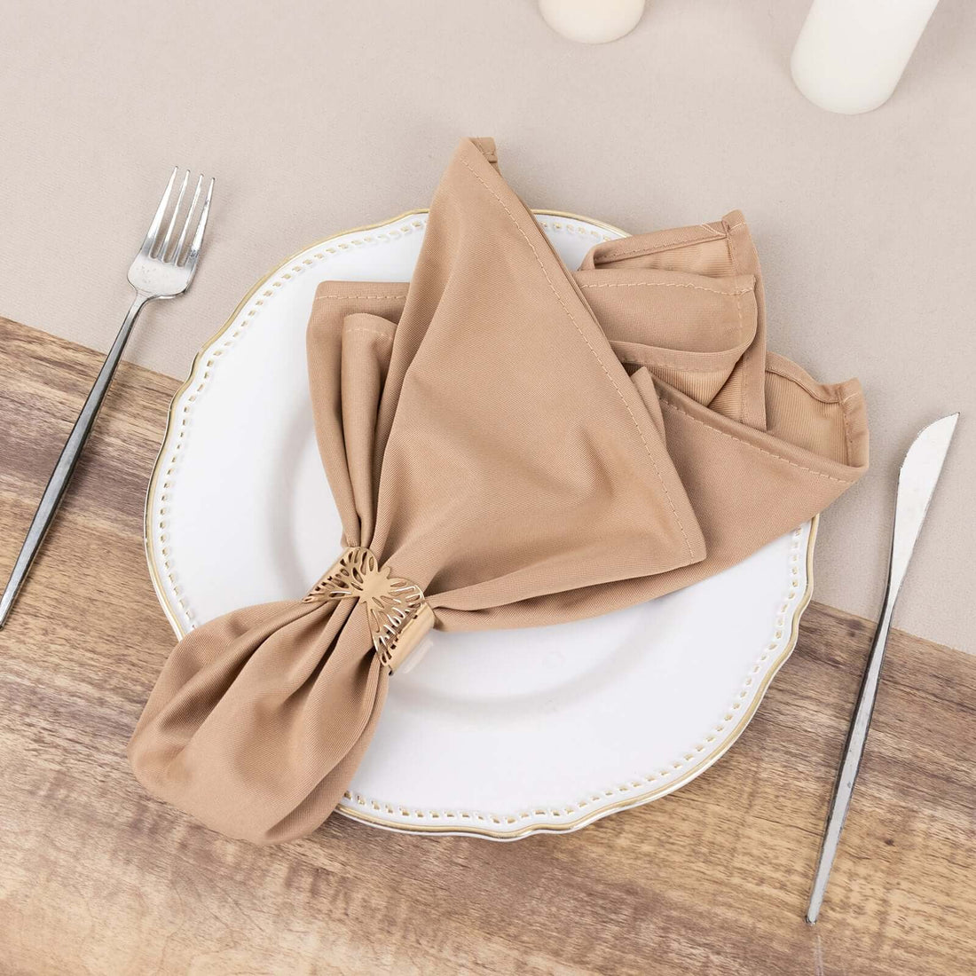 Brown cloth napkin elegantly tied on a white plate with silver cutlery.