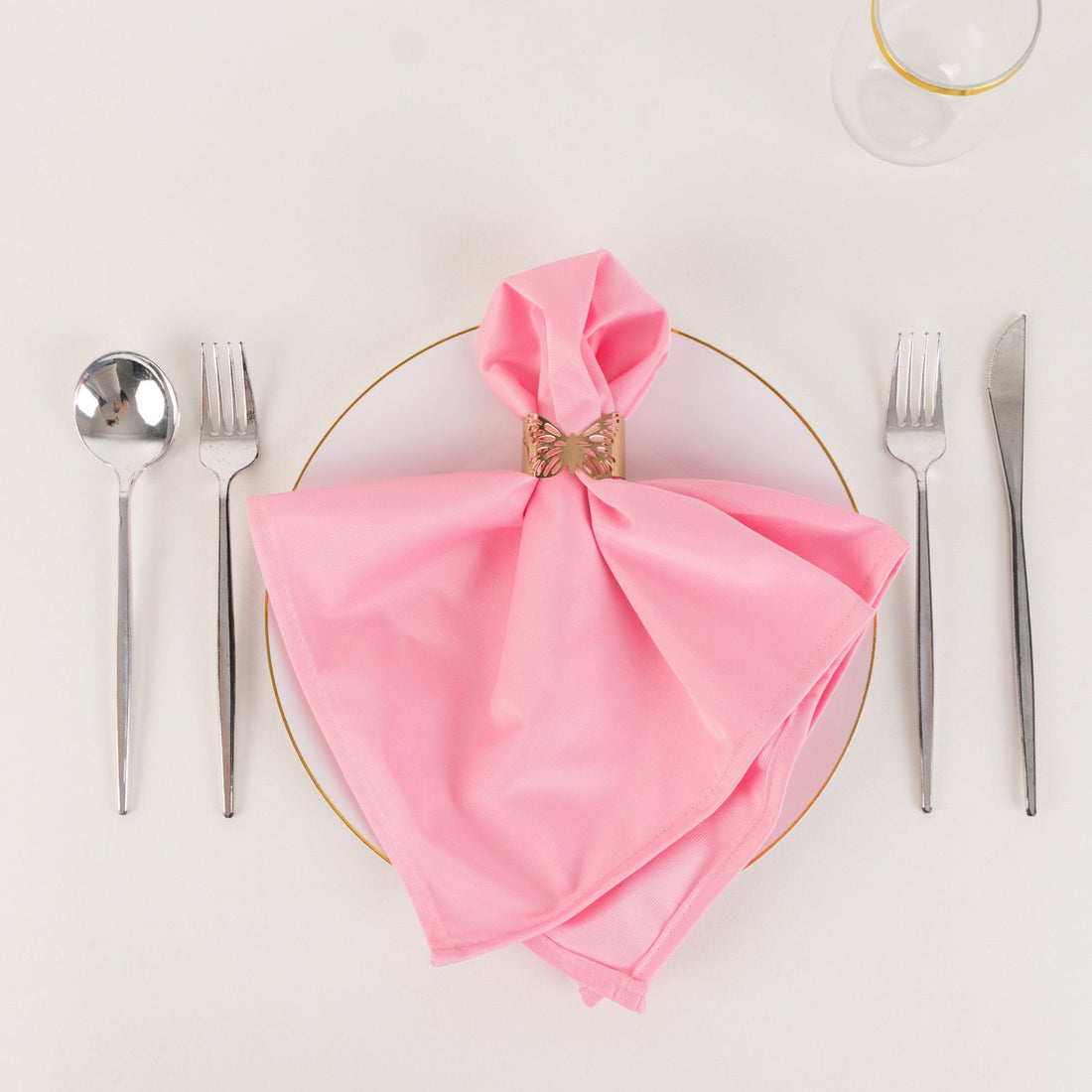 Pink napkin elegantly folded on a plate with silver cutlery arranged around it.