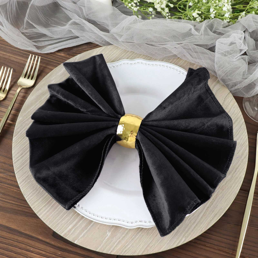 Elegant black napkin tied with a gold ring on a decorative plate.