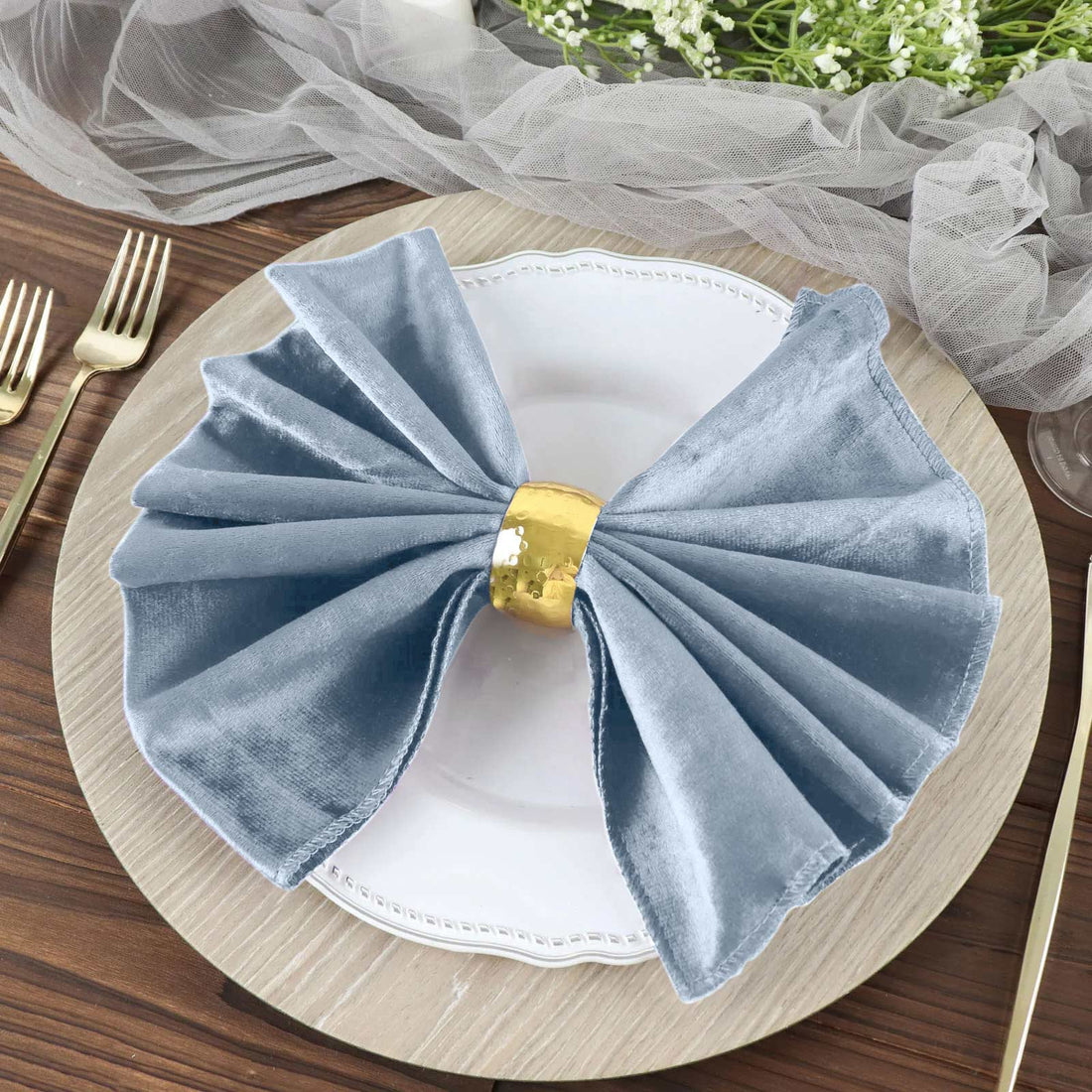 Elegant blue velvet napkin with gold ring on a decorative plate.
