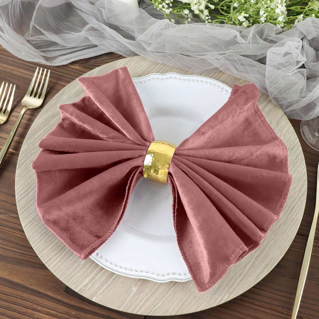 Elegant rose napkin with gold ring on a white plate, styled for dining table.