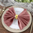 Elegant rose napkin with gold ring on a white plate, styled for dining table.