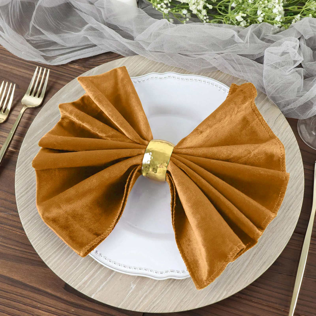 Elegant brown napkin with gold ring on a white plate, styled on a wooden table.